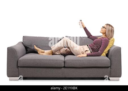 Junge Frau auf einem grauen Sofa mit Fernbedienung Von einer Wechselstromeinheit isoliert auf weißem Hintergrund Stockfoto