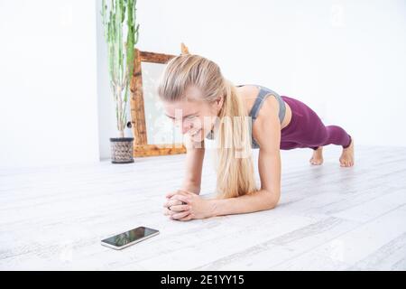 Fröhliche Sportlerin dabei Plank Übung in der Nähe von Smartphone Stockfoto