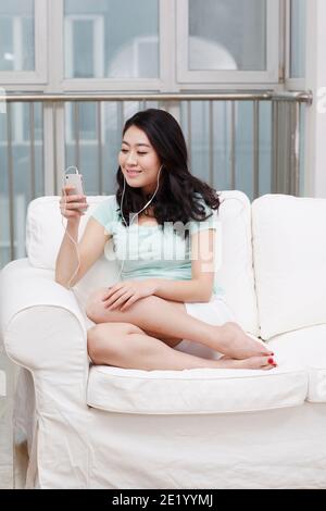 Junge Frau auf einer Couch sitzen, Musik mit einem hören Smartphone hohe Qualität Foto Stockfoto