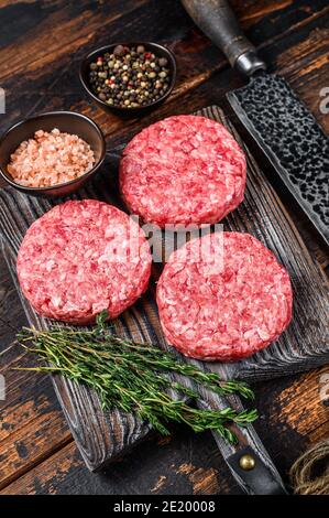 Rohe Steak Burger Patties mit Hackfleisch und Thymian auf einem hölzernen Schneidebrett. Dunkler Holzhintergrund. Draufsicht Stockfoto