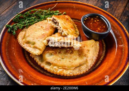 Gebratene Empanadas mit Hackfleisch auf einem Teller mit Chilisauce serviert. Dunkler Holzhintergrund. Draufsicht Stockfoto