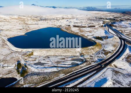 Luftaufnahme eines großen Stausees neben einer großen Doppelstraße an einem verschneiten Tag (A465, Wales) Stockfoto