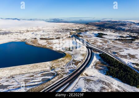 Luftaufnahme eines großen Stausees neben einer großen Doppelstraße an einem verschneiten Tag (A465, Wales) Stockfoto