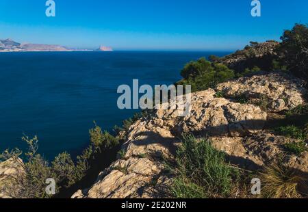 Blick über das Meer auf den Felsen 'Ifach' von Calpe mit steil bewachsenen Klippen vom Naturpark 'Serra Gelada' in Albir, Costa Blanca, Spanien Stockfoto