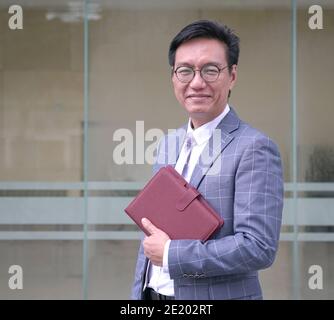 Porträt eines lächelnden asiatischen Geschäftsmannes in Jacke und mit Tagebuch. Stockfoto