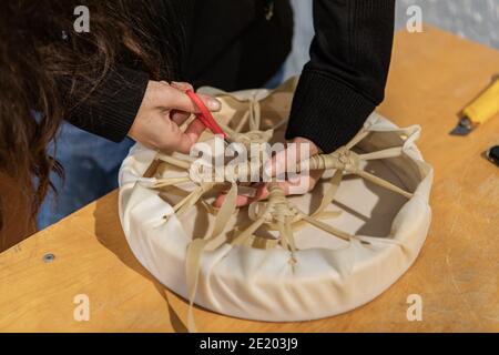 Snapshots aus einem nativen Drum Workshop. Nahaufnahme der Hände einer jungen Frau, die die Enden eines Leders durchschneiden, aus dem ein handgefertigtes Tamburin hergestellt wurde. Stockfoto