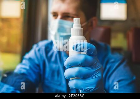 Der junge Kaukasier hält in einer Schutzmaske mit einem medizinischen Handschuh ein Antiseptikum in der Hand. Stockfoto