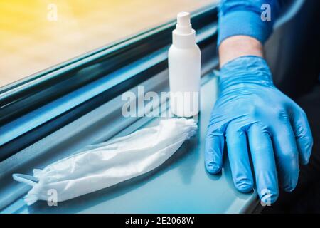 Die Hand einer Person in einem schützenden medizinischen Handschuh liegt neben einer gebrauchten medizinischen Maske und antiseptisch. Hygiene- und Sicherheitskonzept gegen Coronavirus. Stockfoto