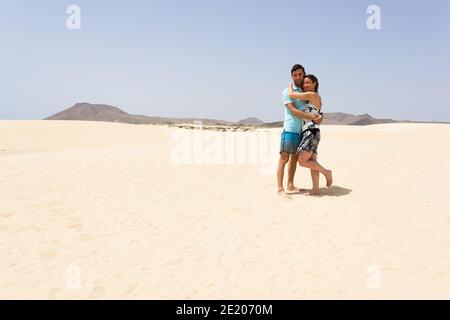 Umarmende Paar posiert in leeren Sanddünen im Corralejo Naturpark. Mann und Frau posieren in der Wüste auf Fuerteventura, Spanien. Sommertourismus Stockfoto