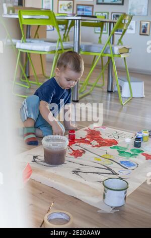 Das Kind zeichnet verschiedene Figuren zu Hause auf ein großes weißes Blatt mit hellen Gouache-Farben. Konzept für Kinder Kreativität, junge Künstler. Kleiner Junge Stockfoto