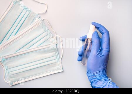 Hand in blauen medizinischen Handschuh hält antibakterielle Desinfektionsmittel auf dem Hintergrund der medizinischen Gesichtsmasken. Hygienische Schutzausrüstung, die vor Infektionen schützt Stockfoto