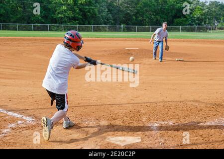 Alabama Dothan Westgate Park Baseballspiel Hardy Field, Vater Pitches Sohn schlägt Fledermaus Schlagschaukeln Praxis Mann Junge, Stockfoto