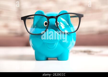 Nahaufnahme ein blaues Sparschwein mit schwarzen Gläsern auf dem Holztisch. Das Symbol des Sparens von Geld und Reichtum finanziell. Stockfoto