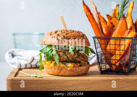 Veganer Linsenburger mit Rucola, Senfsauce, frischem Gemüse und Süßkartoffelfrites auf einem Holzbrett. Veganes Lebensmittelkonzept. Stockfoto