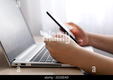 Frau, die Kreditkarten- und Smartphone-Typen auf der Laptop-Tastatur hält. Konzept von Online-Shopping und Bezahlung Stockfoto