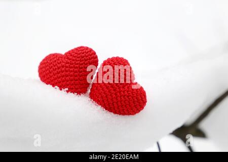 Valentine Herzen im Winterwald, kaltes Wetter. Zwei rote gestrickte Herzen auf verschneiten Ast, Symbol der romantischen Liebe, Hintergrund für Urlaub Stockfoto