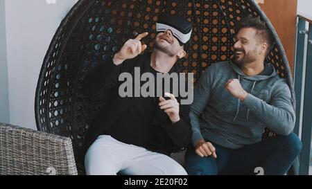 Virtuelle Welt. Fröhliches Gay-Paar trägt VR-Brille und entspannen auf dem Balkon. Hochwertige Fotos Stockfoto