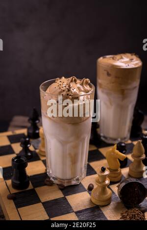 Dalgona Kaffee. Schlagsahngetränk mit Instant-Kaffee beliebt in Korea cremigen Cocktail in hohen Gläsern mit Schach auf Holzchessboard dekoriert Stockfoto