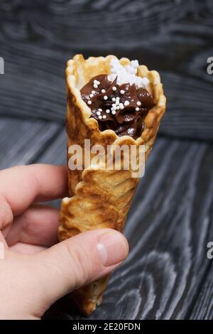 Der Mann hält in der Hand einen Waffelkegel gefüllt mit Schokoladencreme. Dekoriert mit einer Marshmallow Schneeflocke. Stockfoto
