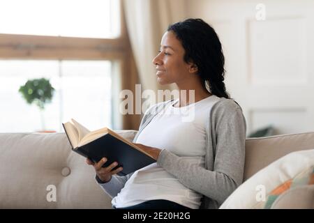 Verträumte junge afroamerikanische Frau, die Papierbuch in den Händen hält. Stockfoto