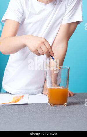 Nahaufnahme eines Jungen in einem weißen T-Shirt wäscht ein Pinsel aus Aquarellfarbe auf blauem Hintergrund Stockfoto