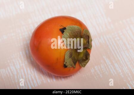 Persimmon mit einem verwelkten Schwanz. Liegt auf einer beigen Oberfläche. Nahaufnahme. Stockfoto