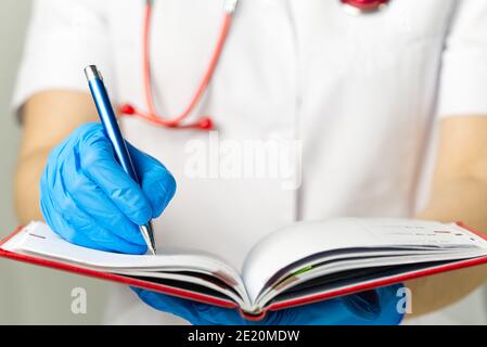 Der Arzt notiert sich im roten Tagebuch Stockfoto