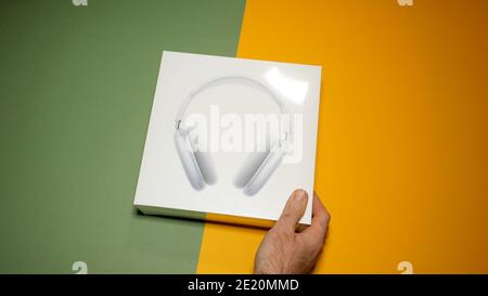 Paris, Frankreich - Jan 7, 2020: POV männliche Hand Auspacken Paket der besten Apple Computers AirPods Max über-Ohr-Kopfhörer auf dem gelben und grünen modernen Hintergrund Stockfoto