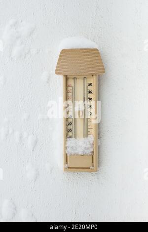 Ein mit Schnee und Eis bedecktes Thermometer für den Außenbereich, das an einer weißen Wand hängt. Winter Herbst. Stockfoto