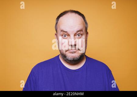 Porträt eines mittleren erwachsenen Mannes mit dumbfounded Blick auf seine Gesicht vor orangenen Studiohintergrund - verwirrter Gesichtsausdruck Stockfoto