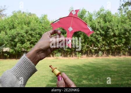 Weiblich, Frau, Mädchen fliegen ein Miniatur-Spielzeug Drachen mit Miniatur niedlichen Spielzeug Spule manjha im Park. Auf dem Festival des Drachenfliegens Festival von uttarayan, makars Stockfoto