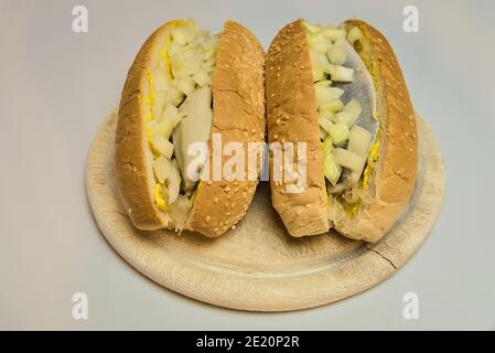 Zwei leckere Hering-Sandwiches mit Sesambrötchen, gelbem Senf, Sauerkraut und weißen Zwiebeln auf runden Holzteller auf weißem Hintergrund Stockfoto
