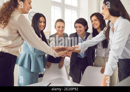 Glückliche junge Geschäftsfrauen oder Firmenangestellte, die die Hände zusammenlegen In Teambesprechung Stockfoto