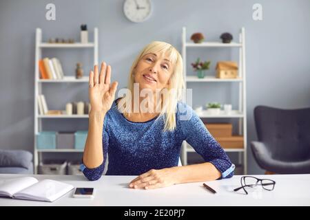 Erwachsene Lehrerin winkt mit der Hand und begrüßt ihre Schüler in einer Online-Lektion während der Quarantäne. Stockfoto