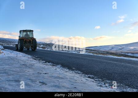 Alter Traktor fährt auf der Old Military Road (R115) in den Wicklow Mountains an einem kalten Winterschneetag, Grafschaft Wicklow, Irland. Schneeräumung. Straßenreinigung Stockfoto