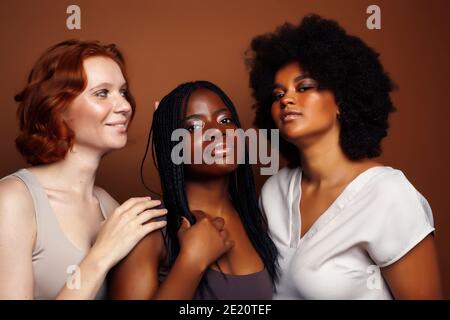 Junge hübsche kaukasische, afro, skandinavische Frau posiert fröhlich zusammen auf braunem Hintergrund, Lifestyle diverse Nationalität Menschen Konzept Stockfoto