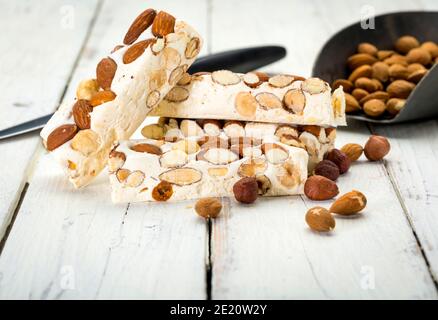 Turron-Blöcke mit Mandeln und Haselnüssen auf rustikalem Holztisch Mit Messer und Schaufel Stockfoto