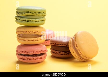 Pastellfarbene französische Macarons mit Himbeer-, Zitronen-, Schokolade- und Pistazien-Aromen auf hellgelbem Hintergrund Stockfoto