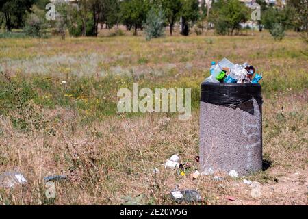 KRYVYI RIH, UKRAINE - AUGUST 2020. Papier- und Plastikflaschen und Tüten in überladenen Mülltonne auf einem Gras im Stadtpark Stockfoto