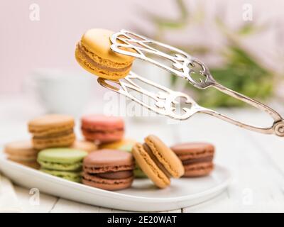 Auswahl an französischem Macarongebäck auf Couchtisch, Schwerpunkt auf einem Zitronengeschmack mit Teigzange, Stockfoto