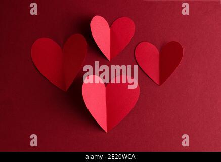 Rote Papierherzen auf dunkelrotem Hintergrund. Valentinstag monochrome Konzept Karte Hintergrund mit leerem Platz für Text. Stockfoto