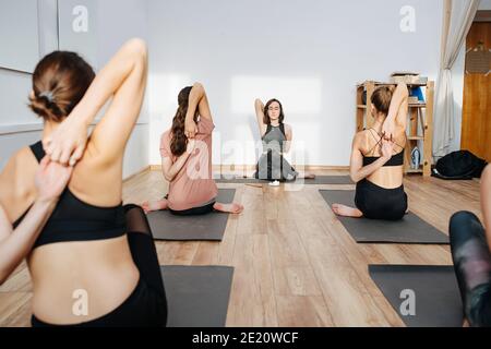 Flexible Frauen üben Yoga in einer Gruppe und verbinden die Finger hinter ihrem Rücken Stockfoto