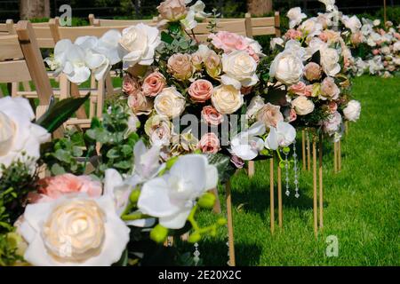 Blumensträuße und weiße leere Holzstühle auf grünem Gras. Dekoration für Hochzeitszeremonien. Stockfoto