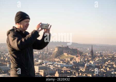 Ein Mann, der ein Foto von der Stadt Edinburgh mit einem Handy macht, von der Spitze der Salisbury Crags, Schottland, Großbritannien. Stockfoto