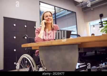 Geschäftsfrau Im Rollstuhl Telefonanruf Tätigen Arbeiten Auf Laptop In Küchenbereich Des Modernen Büros Stockfoto