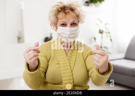 Ältere Frau trägt Gesichtsmaske, medizinische Maske, chirurgische Maske, zwei Hände in weiß, Seitenansicht, Nahaufnahme, Prävention von covid19, Coronavirus Stockfoto