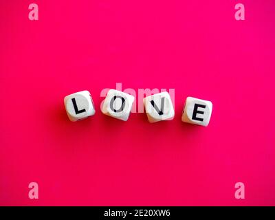 Liebeswort auf Holzblock auf rosa rotem Hintergrund geschrieben, minimalistischer Stil. Liebe, Text ist in schwarzen Buchstaben auf Holzwürfeln geschrieben. Stockfoto