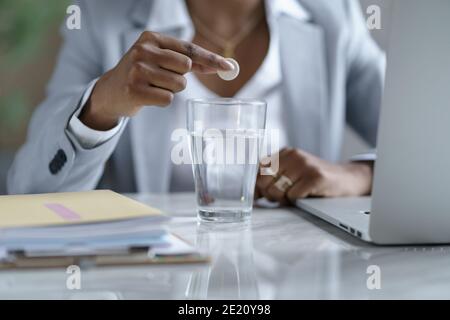 Nahaufnahme afro Geschäftsfrau löst eine Influenza-Pille in einem Glas Wasser, Fokus auf Vordergrund Stockfoto