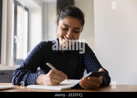 Lächelnde indische Frau machen Notizen mit dem Smartphone Stockfoto