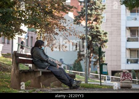 BELGRAD, SERBIEN - 10. OKTOBER 2020: Frau mittleren Alters mit einer Atemmaske sitzend auf einer Bank in einem öffentlichen Park von Belgrad, während der cor Stockfoto